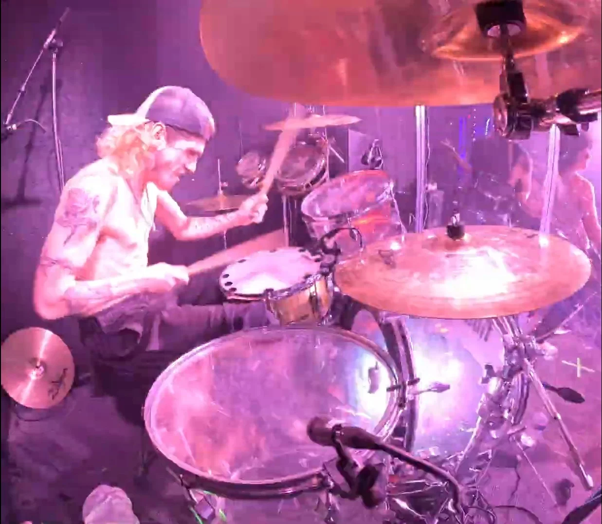 The drummer at the kit in a backwards cap, sticks caught mid-stroke, the whole frame washed magenta by the stage lights